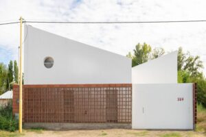 Fachada de casa de 2 niveles color blanco con un muro de celosia de barro. Casa MP por EME arquitectura