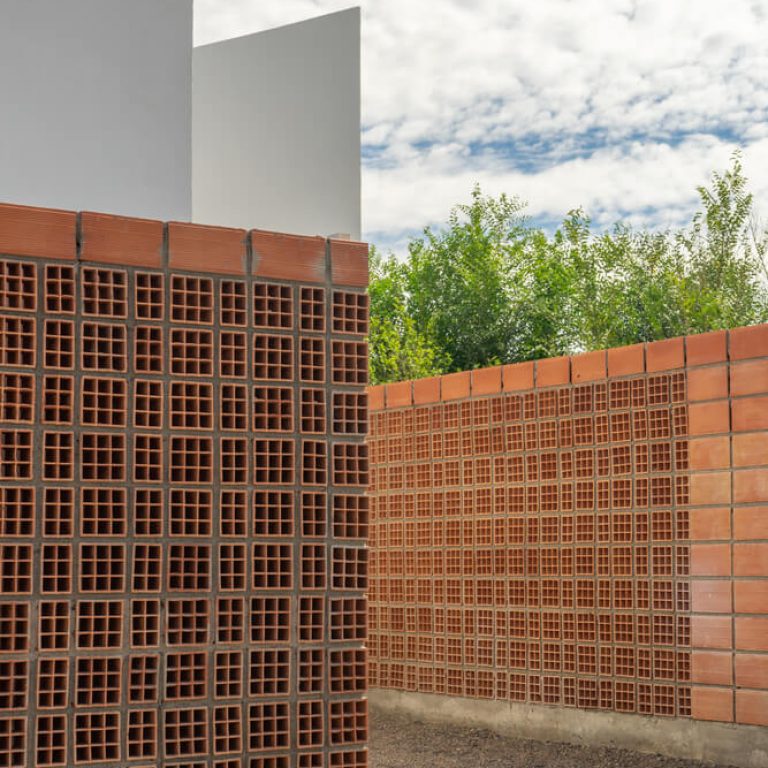Fachada de casa de 2 niveles color blanco con un muro de celosia de barro
