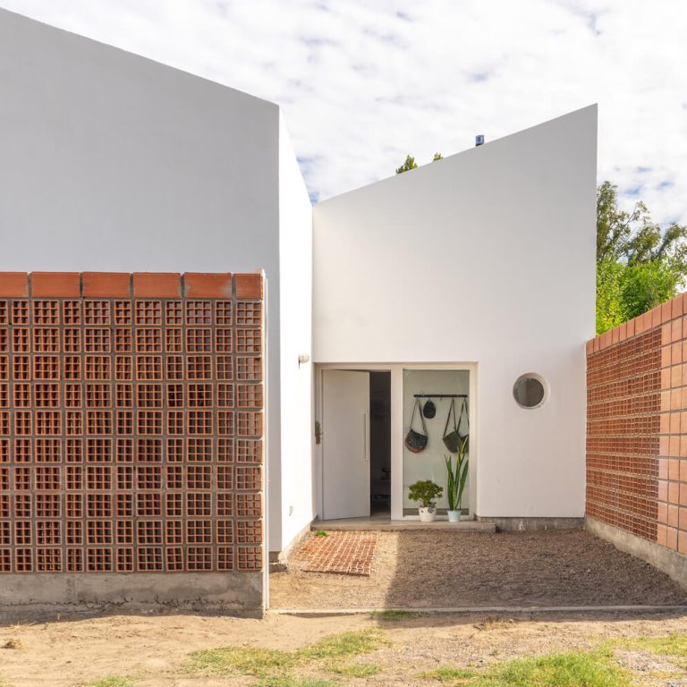 Fachada de casa de 2 niveles color blanco con un muro de celosia de barro