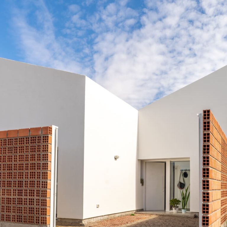 Fachada de casa de 2 niveles color blanco con un muro de celosia de barro