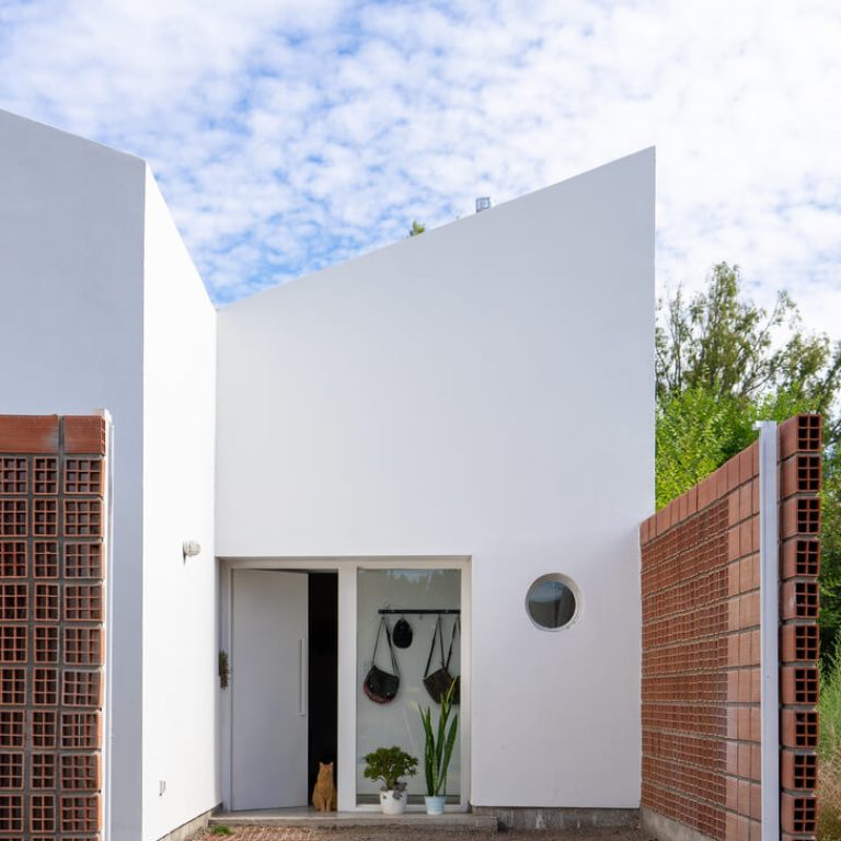 Fachada de casa de 2 niveles color blanco con un muro de celosia de barro