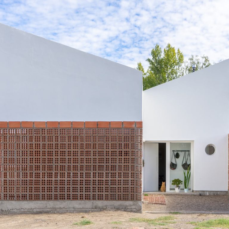 Fachada de casa de 2 niveles color blanco con un muro de celosia de barro