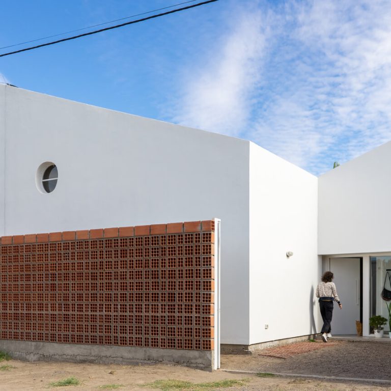 Fachada de casa de 2 niveles color blanco con un muro de celosia de barro