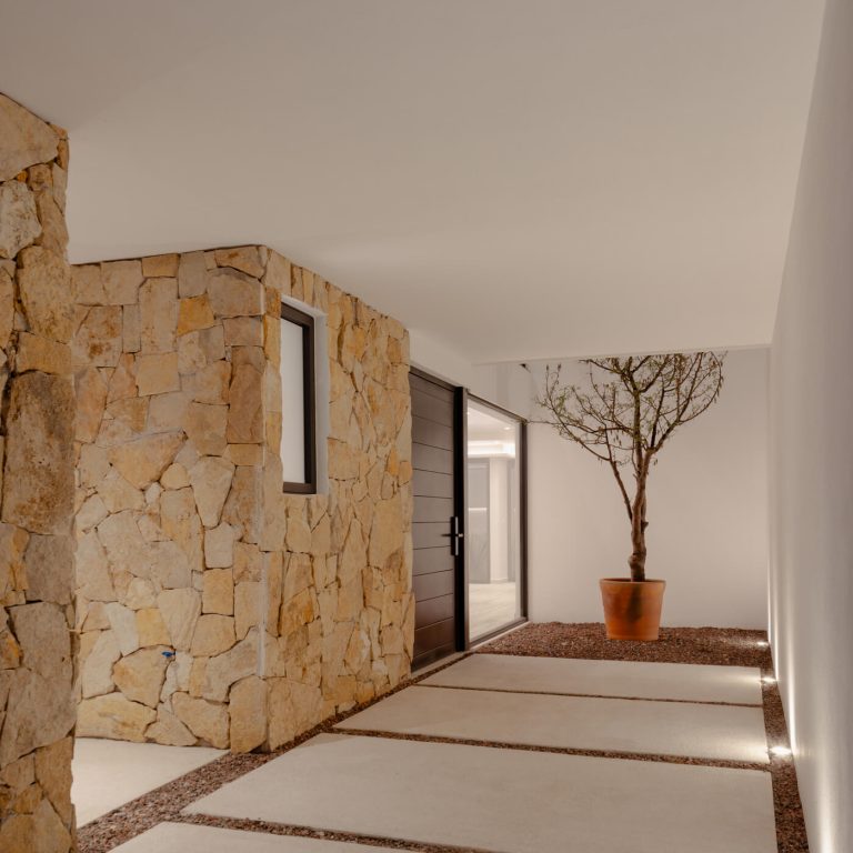 Pasilo ded acceso con un jardin y muros de piedra