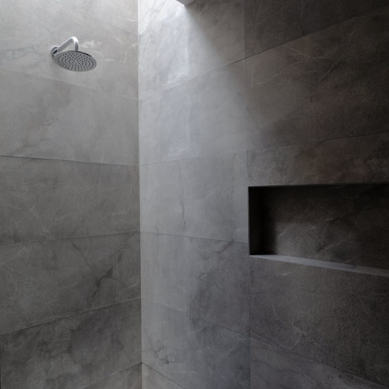 baño moderno con tragaluz en regadera y cerámico en muros color gris