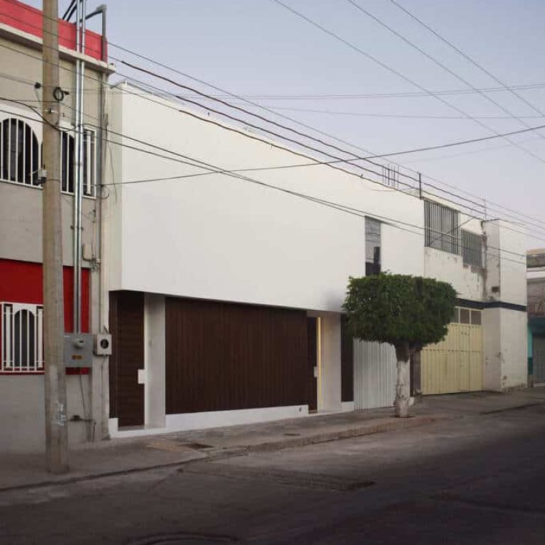 Fachada de color blanco moderna. Un edificio blanco con una puerta roja al costado de la calle.